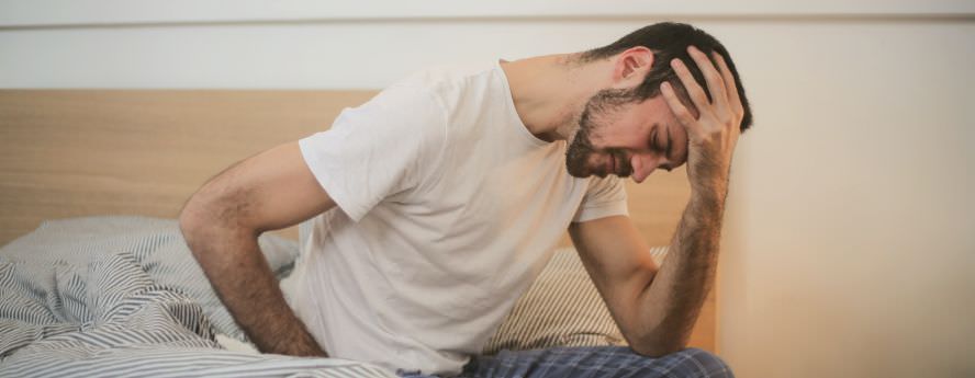 Man Sitting On Bed Suffering From Headache Migraine Feeling Sick