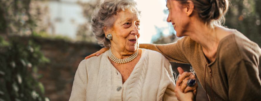 Young Women Smiling And Holding Old Women’s Hand Supporting Her Through Dementia