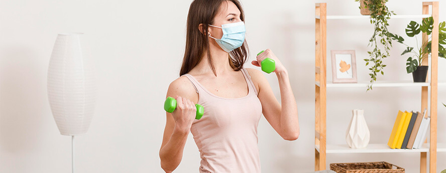 Women Exercising At Home With Green Dumbbells Weight Lifting For Fitness And Health Wearing Face Mask In The Coronavirus Pandemic