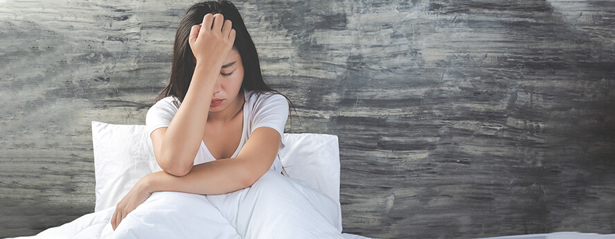 Women In Bed Holding Head While Sick