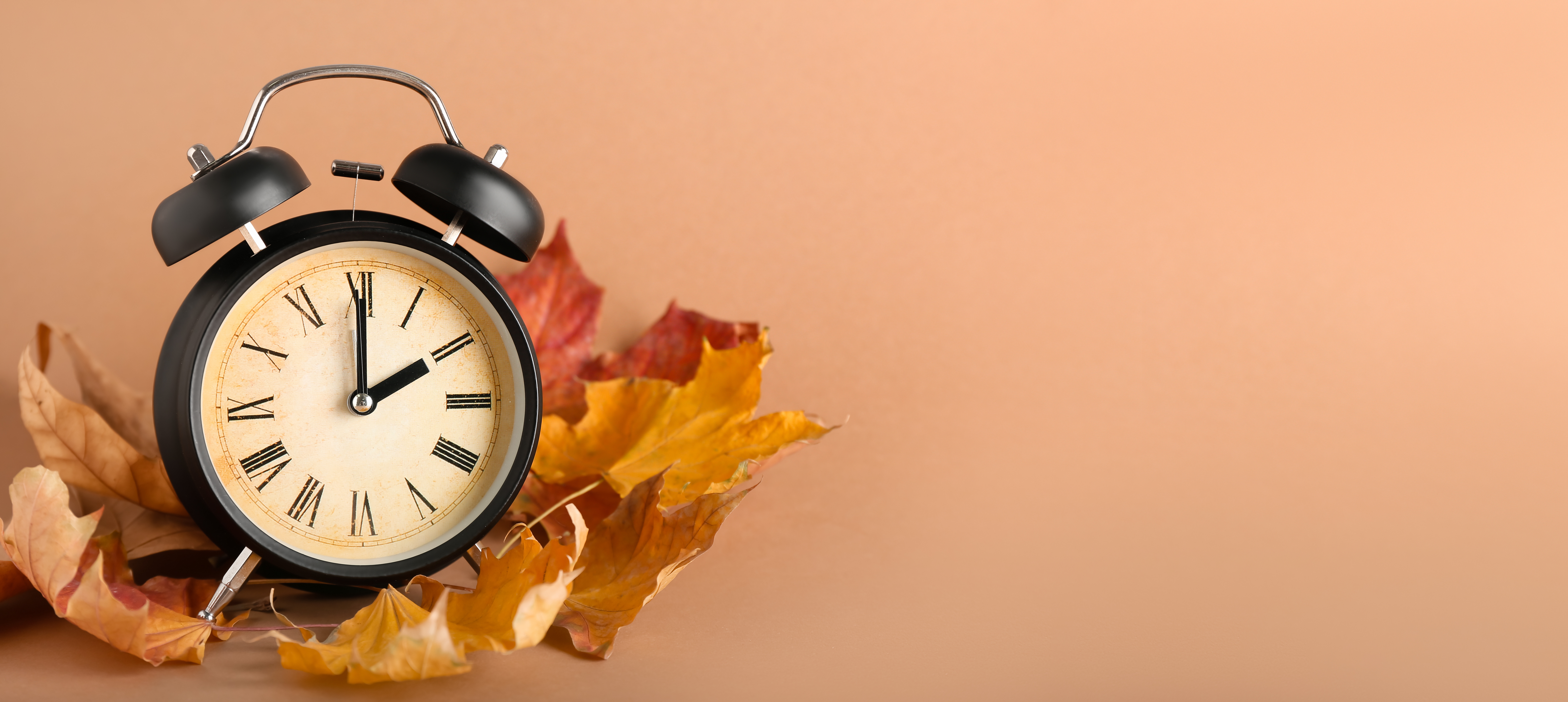 Alarm clock with autumn leaves symbolising seasonal time change and tiredness when clocks go back