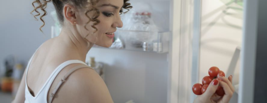 Young Women Smiling Holding Cherry Tomatoes Near Refrigerator Fridge