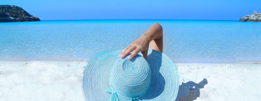 Person Sun Bathing Lying On Sand Beach Wearing Blue Summer Hat And Looking At The Sea